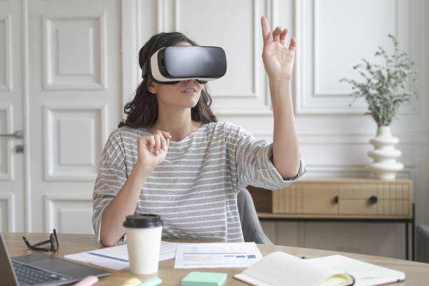 istock Young focused woman wearing virtual reality headset watching 360 degree content at work 1415410678