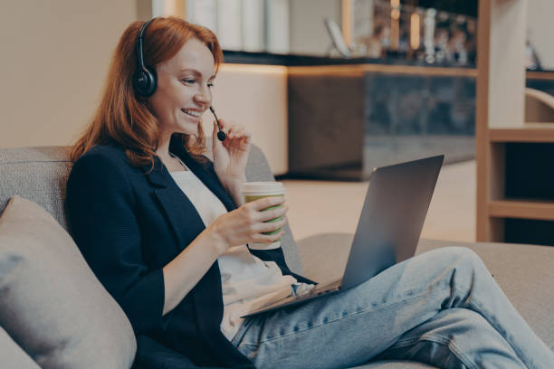 istock Young dispatcher lady working remotely via wireless headset and laptop, sitting on sofa in teahouse 1415412608