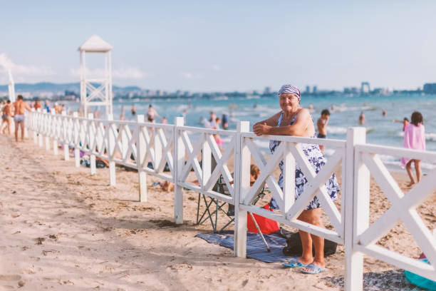 An old woman in a bathing suit and a bandana on the beach of Anapa Old white woman in a bathing suit and a bandana stands leaning on a fence behind the Black Sea and Anapa beach krasnodar krai stock pictures, royalty-free photos & images