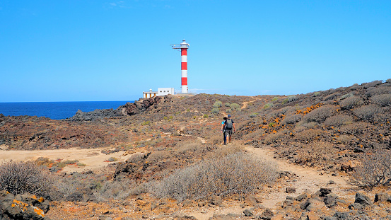Rear view of a couple of hikers walking towards the  lighthouse of Rasca in Tenerife, Canary Islands