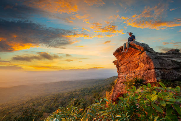 istock man sitting on a cliff,Young man with backpack sitting on rock looking into the landscape. Listening to the silence. Beautiful moment the miracle of nature. 1415422560