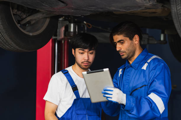 istock Two handsome male mechanics wearing uniform, using tablet, checking or inspecting for fix, repair car or automobile components, working in car maintenance service center or shop. Industry Concept. 1415424343