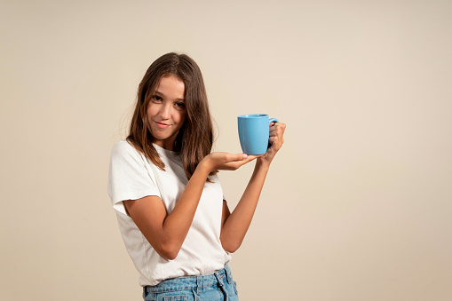 Girl holding a cup of coffee. Coffee break and recreation. Teenager hold a ceramic mug, drink cocoa, coffee or tea. Happy face, positive and smiling emotions of a teenage girl.