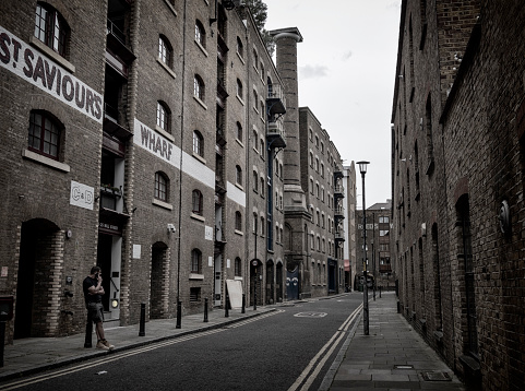 A man talking on his mobile phone in Mill Street by St Saviour's Sufferance Wharf in Southwark, South East London. Once lined with warehouses, the buildings have been converted into trendy apartments. (Subdued colour.)