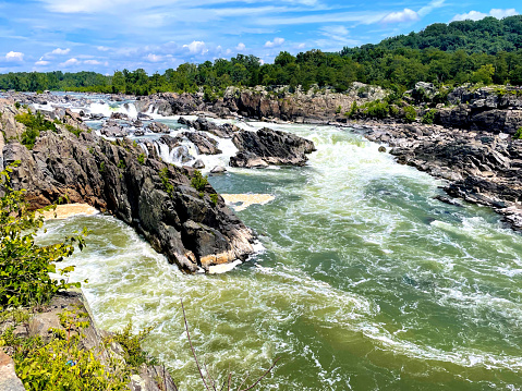 Great Falls, Virginia, USA - August 5, 2022: Powerful water of the Potomac River rushes over the falls at Great Falls Park in Northern Virginia near Washington, D.C., on a sunny day.