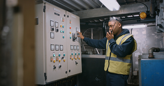 Electrician pressing an electricity distribution board for a scheduled blackout or repairing a tripped power panel. Young electrical expert or employee turning off energy and talking on walkie talkie