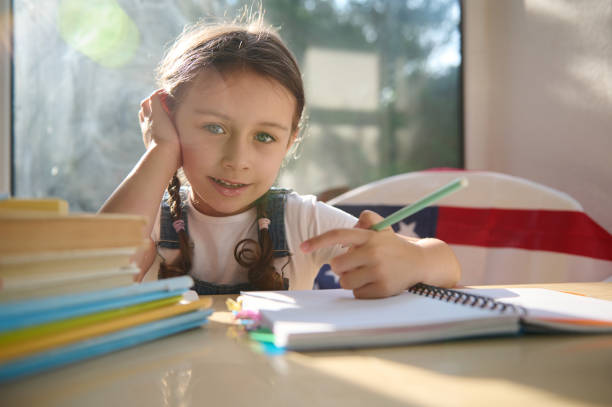 istock Sunbeams fall on a class while schoolgirl studies sitting on the chair with American flag. Happiness to be first grader 1415441012