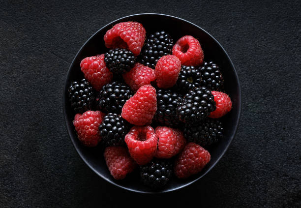 istock Fresh raspberries and blackberries in a ceramic black bowl on a black background 1415441040