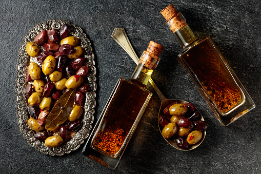 Spicy olives and olive oil on a black stone table. Top view.