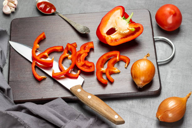 istock Kitchen knife, chopped red pepper, and half pepper on cutting board. Garlic and spoon with tomato sauce. 1415441516