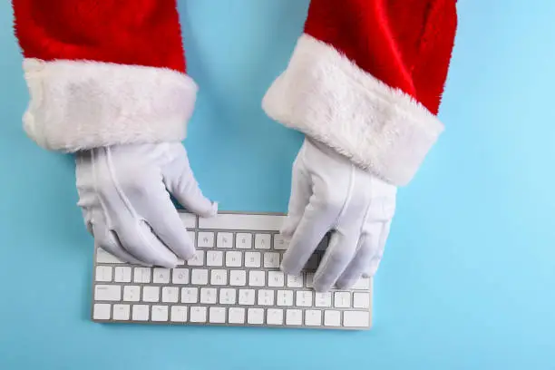 High angle closeup of Santa Claus hands using his computer keyboard on a blue background.