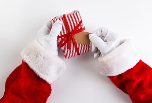 Overhead shot of Santa Claus hands holding a Christmas Present wrpped in red striped paper with a blank gift tag.