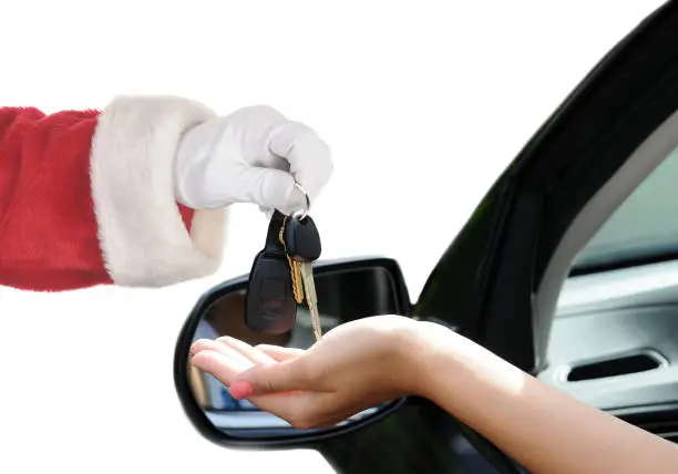 Santa Claus handing over the keys to a new car. Closeup of Santa and a female hand sticking out the window of the vehicle.
