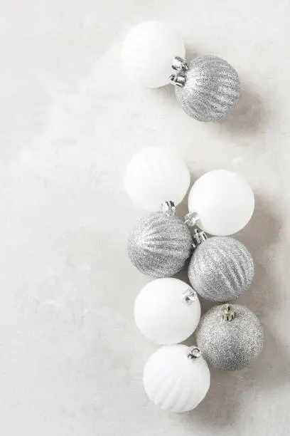 Silver and white Christmas Tree Balls on a light mottled gray surface. Vertical with copy space.