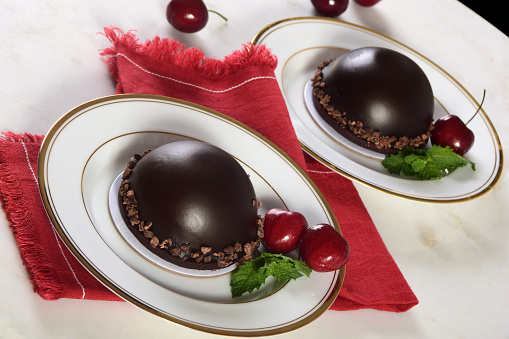 Individual, indulgent and romantic dark chocolate cake bomb filled with chocolate mousse and garnished with cherries and mint.