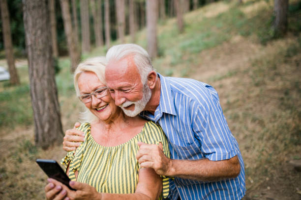 istock Smiling Senior couple using mobile phone in forest 1415447434