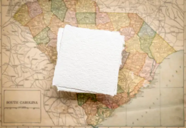 small, blank, square sheet of rough handmade paper floating over vintage defocused map of South Carolina State