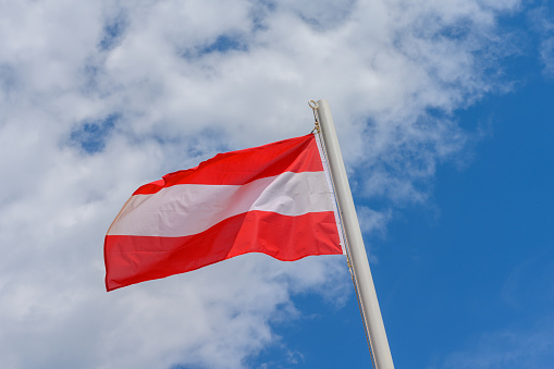 Austrian flag waving in the wind. It is a beautiful sunny summer day, with blue sky and white clouds in the background.