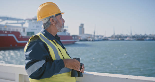 istock Logistics worker working at loading dock by the sea, checking for delivery ship and building a port at the harbor. Male employee doing inspection and looking out for import or export cargo alone 1415450786