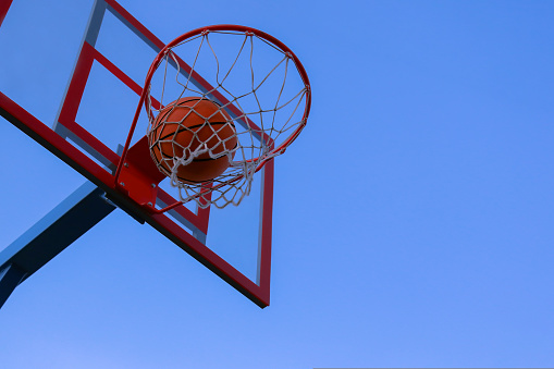 A basketball in a net on a blue sky background. The ball hit the ring. Outdoor basketball court. The basketball flew through the ring, flying in through the basket and the net.