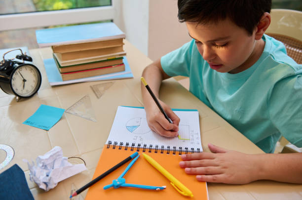 istock Schoolboy does math and geometry homework, draws circles with drawing compass, calculates surface of geometric shapes 1415454127