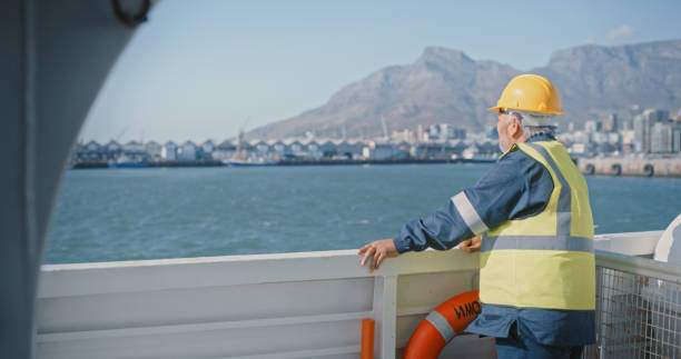 istock Marine engineer taking a break on ship at sea while looking at the dock station and ocean, blue sky or nature copy space background. Senior mechanical supervisor managing operations on a sailing boat 1415456428