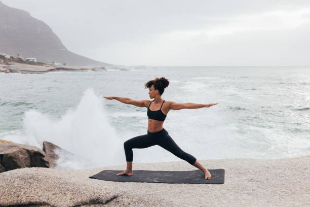istock Woman practicing warrior yoga pose against big waves and an ocean 1415457931