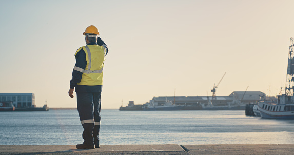 Shipping, freight and logistics with a supervisor standing on the dock in a harbor, looking at the view and waiting for a delivery or shipment. Safety and control in the import and export industry