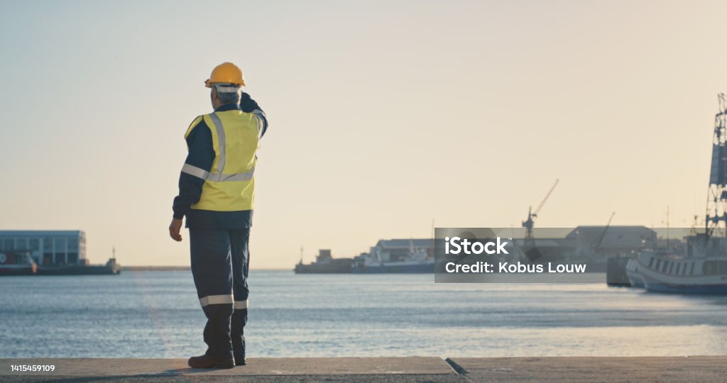 Shipping, freight and logistics with a supervisor standing on the dock in a harbor, looking at the view and waiting for a delivery or shipment. Safety and control in the import and export industry Sea Stock Photo
