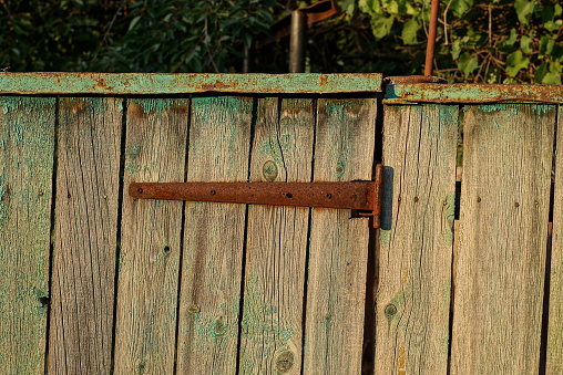 one old rusty metal brown door hinge on gray wooden fence boards in the street