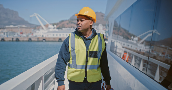 Seaman, engineer and ship mechanic doing maintenance, inspection and repairs while wearing a hardhat and reflective vest. Marine worker, supervisor or manager looking at ocean while doing rounds