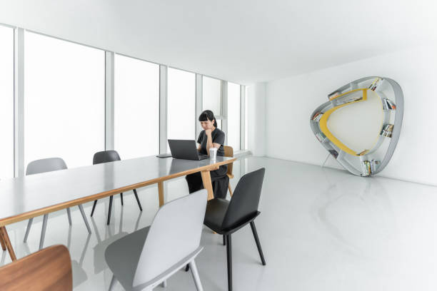 An Asian woman uses a computer for online learning in a spacious, simple and bright conference room