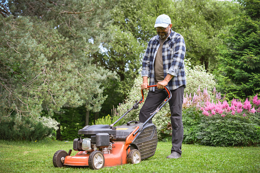 Senior retired male cutting the grass on expansive lawn using yellow zero-turn mower