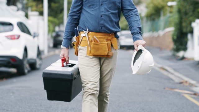 Handyman, construction worker and DIY builder walking down the street with a toolbox and hardhat in hand. Engineer ready to fix, repair and maintain work with his tool belt and building equipment