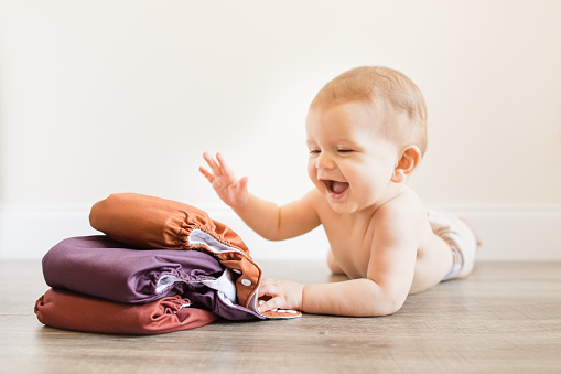 7-Month-Old Baby Boy Wearing a Neutral Colored Reusable Cloth Diaper Laying on His Belly & Playing With His Fall-Colored Cloth Diapers
