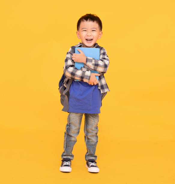 szczęśliwy azjatycki dzieciak trzymający lub przytulający dużą książkę na żółtym tle - child little boys isolated standing zdjęcia i obrazy z banku zdjęć