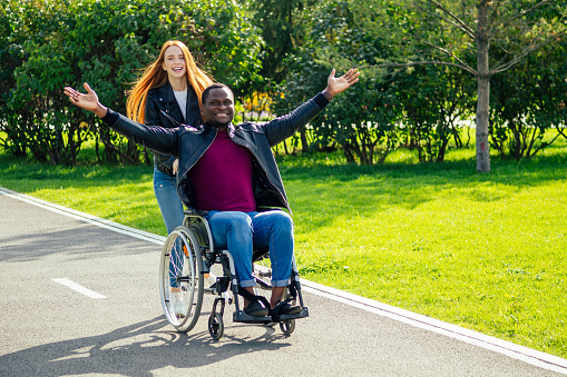 afro american man sitting on wheelchair ,his redhaired ginger girlfriend rolling stroller in autumn park. having romantic date.