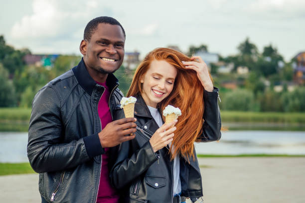 istock Multi ethnic diverse couple eating ice cream in spring autumn park 1415483226
