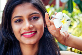 Closeup headshot portrait of attitude confident smiling happy pretty young woman background of blurred trees, plumeria flowers. Positive human emotion facial expression feelings
