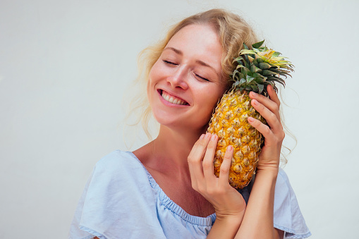 portrait of beautiful blond hair woman with blue eyes holding pineapple on white background.detox and allergy to tropical products