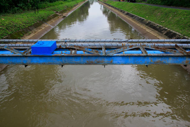 A close-up perspective of a narrow concrete channel with water flow, bordered by green grass, illustrating outdoor irrigation or drainage systems.