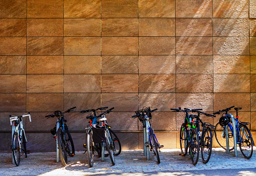 Cambridge, Massachusetts, USA - August 15, 2022: A variety of eight bicycles parked at individual bike racks against an orange-yellow building wall in Harvard Square.