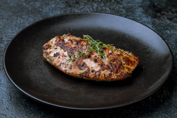 istock Grilled chicken Breasts on black plate on dark stone table macro close up 1415488714