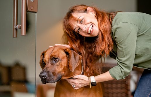 Portrait of a smiling woman petting her dog while standing together at the front door of her house