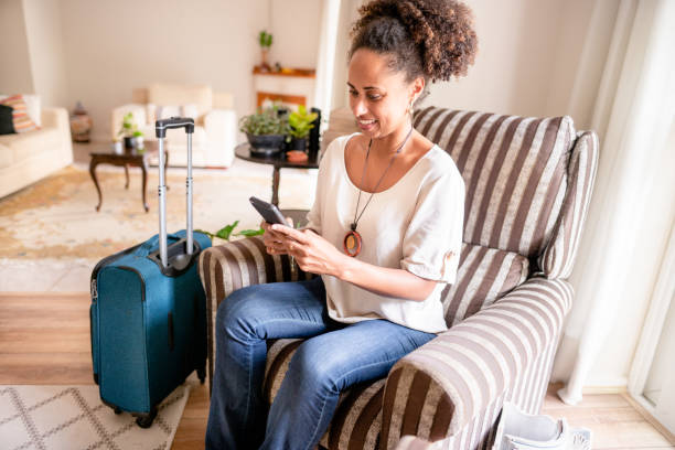 istock Smiling woman using a phone while sitting with her bags in her hotel 1415491432