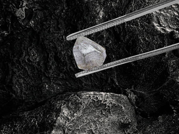 istock Natural diamond held in tweezers on black coal background 1415492034