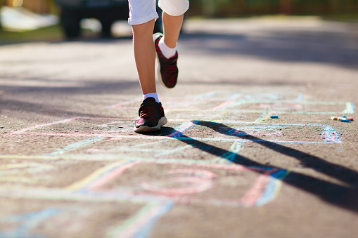 Kids play hopscotch in summer park. Healthy active outdoor game. Children playing and drawing with chalk on suburban city street. Boy and girl jump. Hop scotch fun for young child. Kid jumping.
