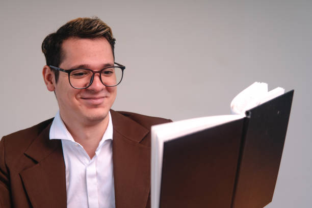 istock A blond, Caucasian man reading a book with a happy face. Man enjoying while he reads a book. Man in a suit reading a black book. 1415501726