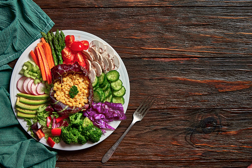 Vegan food themes. Healthy eating and diet concepts. Top view of spring salad shot from above on rustic wood table with copy space Included ingredients: Chicken, tomatoes, broccoli, lettuce, bell peppers, mushroom, carrots, radicchio, almonds.