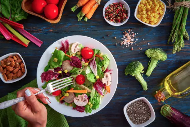 Vegan food themes. Table top view of colorful and healthy fresh salad on rustic wood table. Included ingredients: Chicken, tomatoes, broccoli, lettuce, bell peppers, mushroom, carrots, radicchio, almonds.